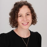 A woman with curly brown hair smiles warmly, wearing a black top and necklace, in a medbridge healthcare education setting.