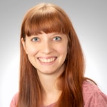 A woman with long red hair smiles in a pink top against a gray background, embodying Medbridge's vibrant digital healthcare spirit.