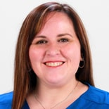 A confident woman with long brown hair and hoop earrings smiles at the camera, embodying the empowerment from digital healthcare experiences with Medbridge.