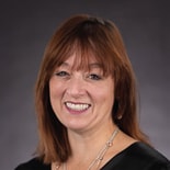 A smiling woman with brown hair represents modern digital healthcare, wearing a black top and medbridge necklace.