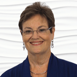 A confident woman with short brown hair and glasses stands against a white background, representing hybrid care in healthcare education for medbridge.