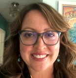 A smiling woman with glasses and turquoise earrings poses in front of colorful artwork, representing medbridge's vibrant culture.