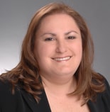 A smiling person with shoulder-length brown hair in a black blazer represents modern digital healthcare for medbridge.