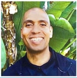 A person smiling outside with big green leaves behind them, wearing a medbridge t-shirt.