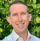 A smiling man in a white shirt stands before green leaves, reflecting the positive impact of medbridge healthcare education.
