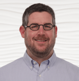 A smiling person in a striped shirt stands in front of a wave pattern backdrop, reflecting hybrid care and digital healthcare themes for medbridge.