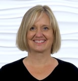 A smiling person with short blonde hair, wearing a black top, stands against a wavy patterned white wall, representing medbridge's innovative patient care software in healthcare education.