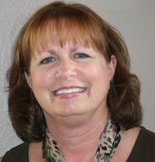 A smiling individual with brown hair and a patterned scarf represents medbridge's healthcare training compassion.