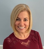 A woman with straight blonde hair in a burgundy lace top smiles at the camera against a light blue background, representing medbridge.
