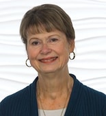 A smiling woman with short hair and hoop earrings wears a teal top against a white background, representing medbridge's spirit of healthcare education.