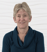 A smiling person with short, light hair in a blue sweater stands against a textured white background, reflecting the positivity associated with medbridge healthcare training.