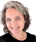 A woman with partly gray hair smiles warmly, wearing a black top with floral shoulder patterns, embodying medbridge's healthcare training spirit.