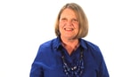 A confident woman with shoulder-length blonde hair smiles, wearing a blue shirt and layered necklace against a white background, embodying digital healthcare inspiration for medbridge.