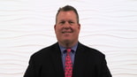 A person in a suit with a pink tie stands against a wavy textured wall, highlighting medbridge's innovative role in modern healthcare education.