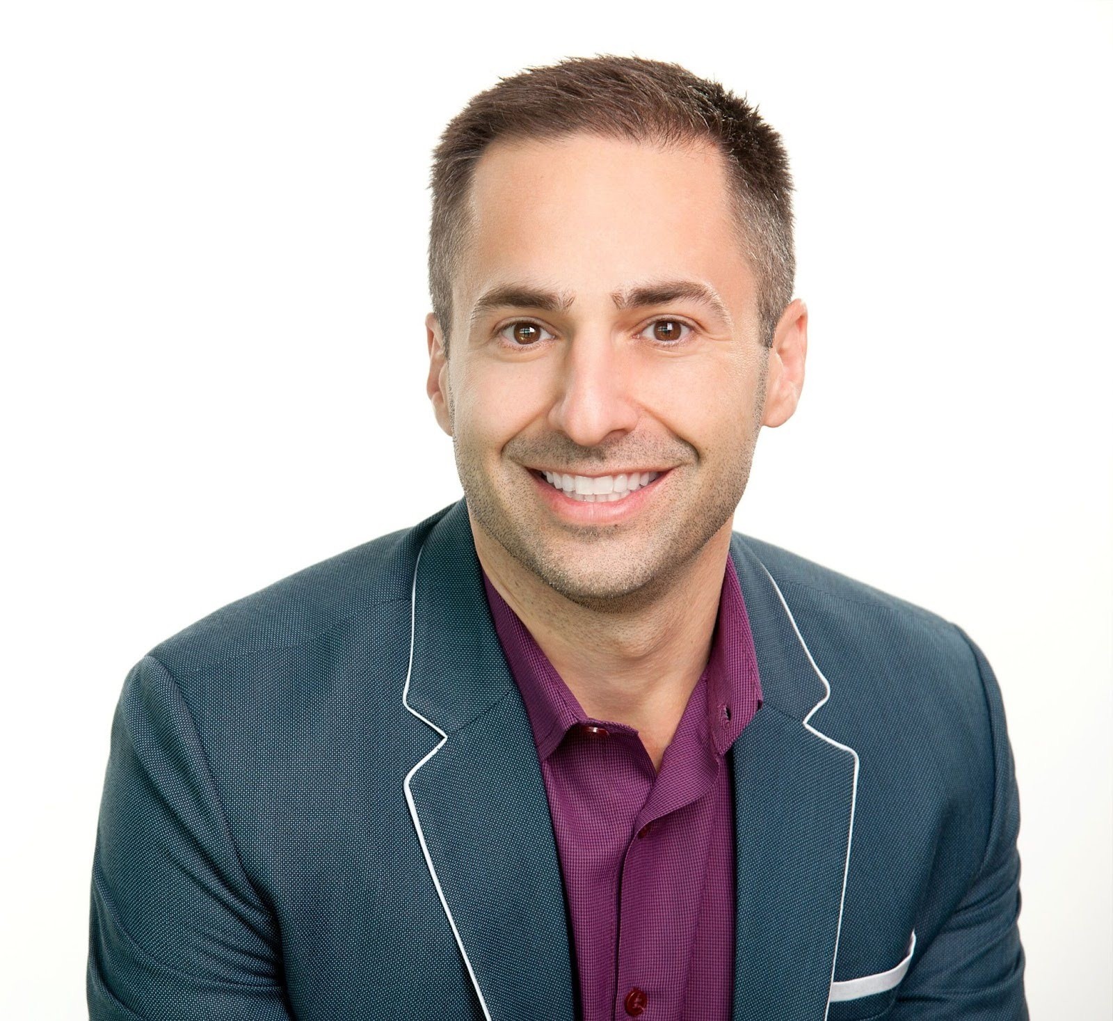 Smiling man in a dark blazer with white trim and purple shirt, against a white background, representing medbridge innovation.