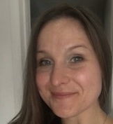 A woman with long brown hair smiles at the camera indoors near a white wall, showing medbridge digital healthcare professionalism.