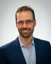 A smiling man in a navy blazer and glasses represents Medbridge's professional healthcare innovation.