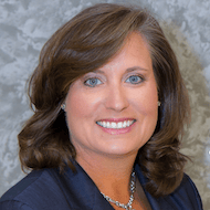 A smiling woman with brown hair and a dark blazer represents Medbridge's healthcare training.