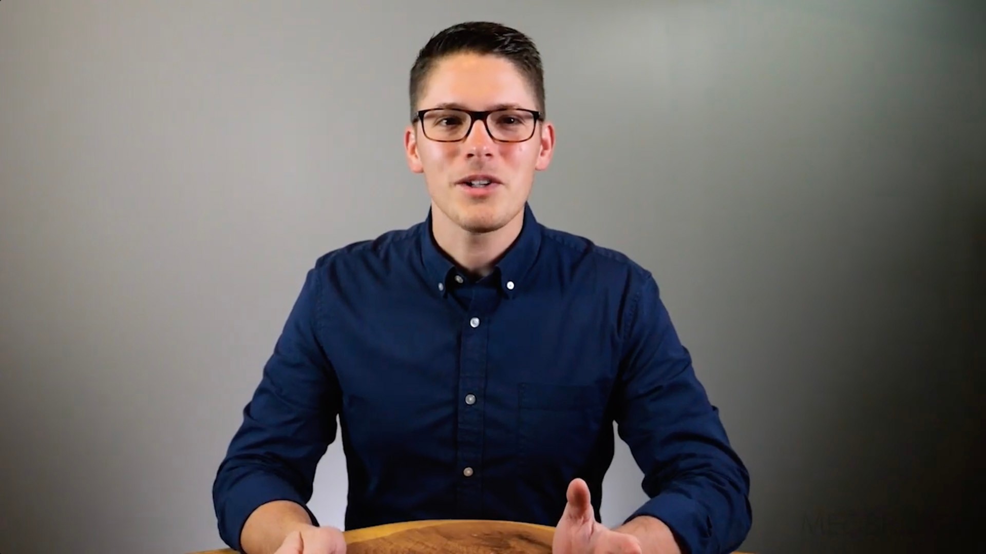 A person in glasses and a navy shirt discusses digital healthcare advancements at a table.