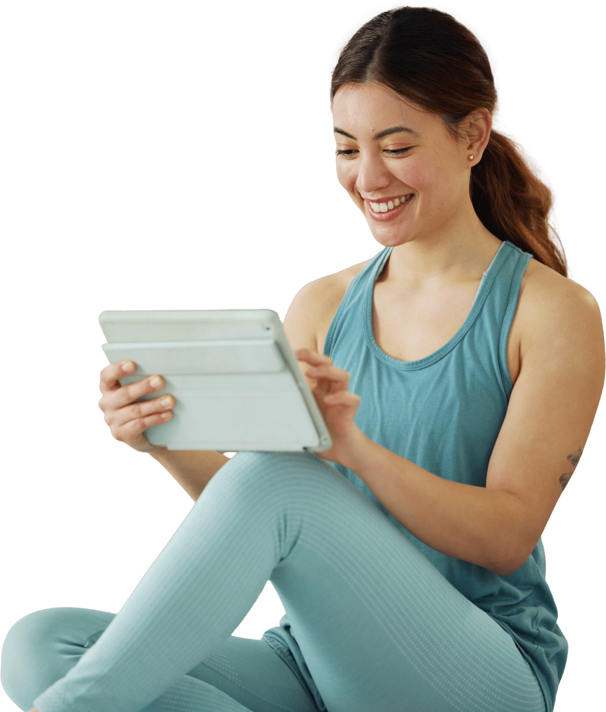 A woman in a teal tank top and leggings smiles while using a tablet with Medbridge.