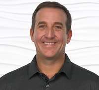 A person in a dark polo shirt smiles against a wavy white background.