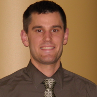 A confident professional in digital healthcare stands before a beige wall, wearing a brown shirt and patterned tie, likely representing medbridge.