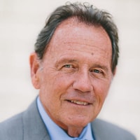 A person in a gray suit and blue shirt smiles slightly with a light blurry background, representing medbridge.