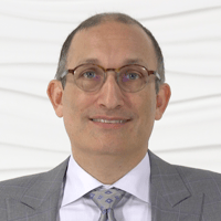 Man in a gray suit and glasses smiling against a white textured background for medbridge.