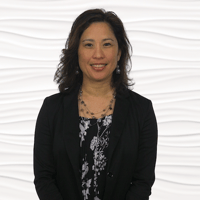A person in a black blazer and patterned blouse smiles against a wavy white backdrop.