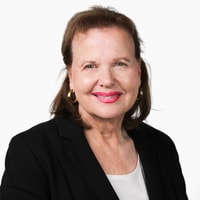 A woman with brown hair wearing a black blazer, white top, and gold hoop earrings smiles at the camera, representing medbridge and digital healthcare.
