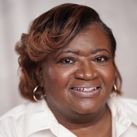 Person smiling with styled hair, in a white shirt and hoop earrings, on a plain backdrop for the medbridge campaign.