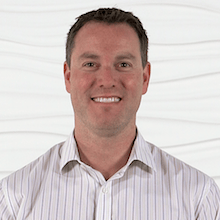A smiling person in a striped shirt stands against a textured white background.