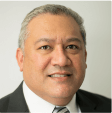 A confident man in a suit smiles in a portrait, representing digital healthcare expertise at medbridge.