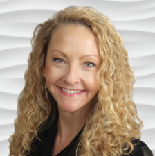 A smiling person with long curly hair stands before a wavy white background, representing the future of digital healthcare with Medbridge.