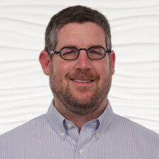 Man with glasses and a beard in a striped shirt smiles confidently, hinting at digital healthcare interest, for medbridge.