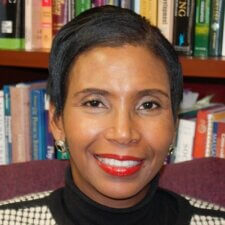 A smiling person with short dark hair and red lipstick stands before a bookshelf, symbolizing their passion for healthcare education at medbridge.