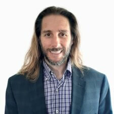 A person with long hair and a beard in a checked shirt and blazer smiles, illustrating medbridge's blend of tradition and modern healthcare.