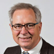 An elderly man with glasses and a suit smiles warmly, representing hybrid care and medbridge healthcare education.
