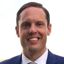 A smiling man with short dark hair in a blue suit and tie represents the future of digital healthcare, embodying Medbridge's vision.