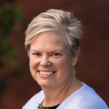 A smiling person with short blond hair in a white top stands outside, symbolizing medbridge's healthcare education.