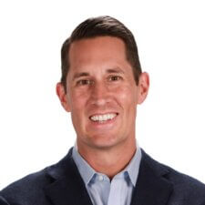 Individual with short dark hair in a dark jacket and light blue shirt, smiling at the camera for medbridge.