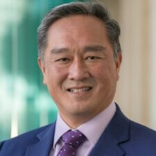 A person in a blue suit and purple tie smiles at the camera, representing Medbridge's professionalism.