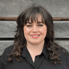 A woman with dark hair and bangs, in a black shirt, smiles warmly against a wooden background; her interest in healthcare education aligns with medbridge values.