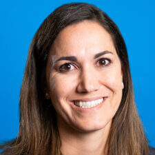 A person with long brown hair smiles against a blue background, representing medbridge's patient care software.