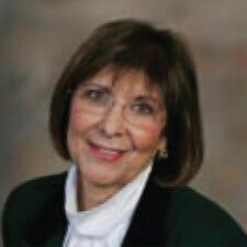 A professional woman with short brown hair and glasses, wearing a dark jacket and white blouse, embodies Medbridge's innovative digital healthcare spirit.