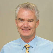 A smiling man in a blue shirt and yellow-striped tie represents the positive impact of hybrid care on healthcare education, as seen with medbridge.