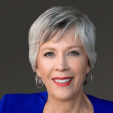 A smiling person with short gray hair, red lipstick, and a blue top represents Medbridge's welcoming approach to digital healthcare innovations.