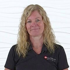 A woman with curly blonde hair in a black polo stands before a wavy white wall, representing medbridge's healthcare education focus.