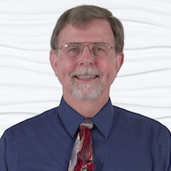 A smiling man with glasses, a beard, and a blue shirt represents expertise in digital healthcare at medbridge.