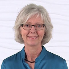 A smiling woman with short gray hair and glasses, wearing a teal blouse, against a white background represents her passion for healthcare education at medbridge.